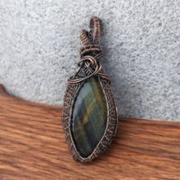 A large oval Tiger's Eye cabochon with golden-brown banded luster. It is encased in a heavy copper wire wrap with a dark oxidized finish. The wirework includes thick woven layers and multiple scrolls near a large integrated bail.