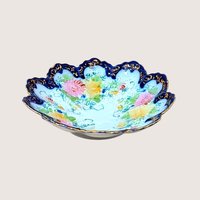 Scalloped porcelain bowl with a deep cobalt blue rim and intricate gold filigree. The interior features hand-painted pink and yellow floral bouquets with delicate green vines on a white ground.