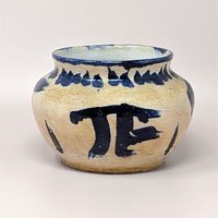 Hand-thrown pottery bowl with a globular shape and a sandy, textured tan glaze. Featuring bold, gestural cobalt blue brushstrokes including a large "PI" or "TF" symbol and a saw-tooth rim pattern.