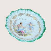 Antique Dresden porcelain bowl with a scalloped edge and green ombré rim. Center features a classical scene of a woman and a cherub with floral garlands. Gold filigree accents. 9.25 inches wide.