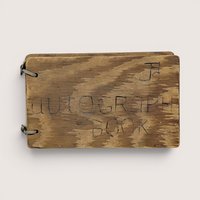 A small, rectangular autograph book with a natural wood grain cover. The words "Autograph Book" are hand-carved into the wood. Two metal rings bind the pages on the left. Rustic, weathered texture with a warm honey-oak finish.