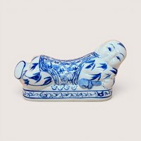 A horizontal porcelain headrest shaped like a reclining child. Featuring a crisp white ground with traditional cobalt blue floral and scroll patterns. Glossy vitrified texture with hand-painted facial details.