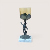 A 9-inch vintage candle holder featuring a dark cast metal cherub figure standing on a white marble square base, supporting a translucent amber glass cup.