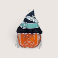 A vibrant stained glass suncatcher of a jack o' lantern wearing a black and teal witch's hat with a silver bat and wire fringe on a neutral background.