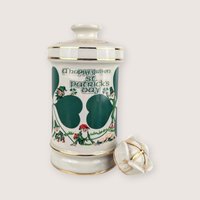 White ceramic Old Commonwealth Flowers of Ireland empty decanter with a green St Patricks Day graphic and broken stopper.