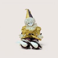 A large porcelain clown doll in a metallic gold and burgundy costume, wearing a tall pointed hat and featuring a white curly wig and hand-painted face.
