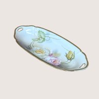 An oval porcelain tray with painted roses and gold trim, angled on a beige background.