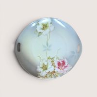 A round porcelain handled plate with painted pink and white floral details, centered on a beige background.