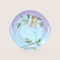 A round porcelain handled plate with painted pink and white floral details, centered on a beige background.