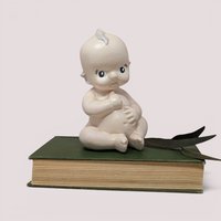 Vintage matte ceramic Kewpie baby doll talcum powder shaker seated with side-glancing eyes and a small chip on its ear.
