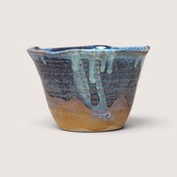 A 1980s studio pottery bowl with a blue and sand colored drip glaze and a wavy rim on a plain background.