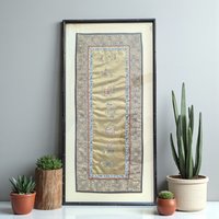 A vertical rectangular silk panel featuring intricate hand-stitched embroidery. The design shows traditional motifs on a shimmering silk background. The textile is housed in a dark wooden frame with a slim profile. The silk appears smooth and taut, while the frame shows minor surface scuffs consistent with age.