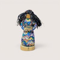 A handcrafted textile doll with long black hair holding a small basket, centered on a beige background.