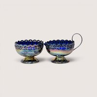 A silver-plated cream and sugar set with ornate openwork details showcasing deep cobalt blue glass liners inside.