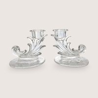A pair of vintage clear glass cornucopia or leaf-shaped single candlestick holders, centered on a beige background.