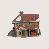 Department 56 Bluebird Seed and Bulb ceramic garden shop building with a stone chimney and snow on the roof.
