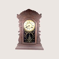 Antique Waterbury Tampa gingerbread parlor clock with an intricately carved walnut case and gold stenciled glass door.