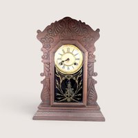 Antique Waterbury Tampa gingerbread parlor clock with an intricately carved walnut case and gold stenciled glass door.