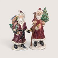 Pair of vintage hand-painted Old World Santa figurines in red coats carrying trees and toys on snowy bases.