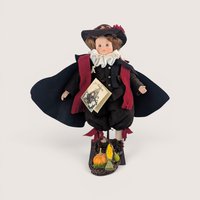 A 12.5-inch vintage Mary Michaud porcelain and fabric Samuel Eaton silhouette doll wearing a dark cape and pilgrim attire on a stand.
