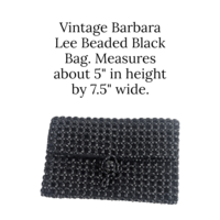 A horizontal view of a vintage black evening clutch covered in a dense pattern of shimmering black beads. The bag has a clean, soft-edged silhouette without a visible metal frame. The front features a fold-over flap with a discrete, bead-covered clasp located in the center for a seamless, elegant look.