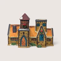 1991 Lemax porcelain village house with stone walls, orange roof, and Christmas wreaths on a plain linen background