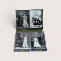 Collection of four vintage black-and-white cabinet card photographs depicting formal family and couple portraits from the late 19th or early 20th century, arranged in a two-by-two grid on a green fabric surface, centered on a plain linen background.