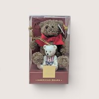 Boxed collector's set titled "AMERICAN BEARS" celebrating the Teddy Bear 100th Anniversary, containing a small brown plush teddy bear wearing a large red bow paired with a white porcelain teddy bear figurine dressed in a patriotic red, white, and blue vest with wire-rimmed glasses, centered on a plain linen background.