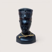 Vintage hand-carved dark wooden bust depicting Queen Nefertiti wearing a traditional high crown, accented with a small piece of natural twine tied in a knot around the neck, centered on a plain linen background.