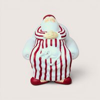A vintage Department 56 Winter Silhouettes "Cat Nap" Santa figurine on a soft pink background. The matte white porcelain sculpture shows Santa sleeping soundly in a large armchair wearing red-striped pajamas with a white cat napping on his lap.