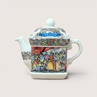 A vintage Sadler porcelain castle themed teapot on a soft pink background. The square cream colored teapot features a detailed double sided illustration of King Arthur's court at Camelot and Sir Lancelot with stone wall borders and a matching lid.