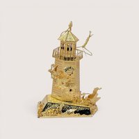A 1998 Danbury Mint North Pole Lighthouse Christmas ornament on a soft pink background. The fine filigree brass ornament is plated in bright 23kt gold, featuring a detailed lighthouse surrounded by a miniature flying Santa and reindeer team.