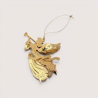 A 1999 Danbury Mint Millennium Angel Christmas ornament with its box on a soft pink background. The fine filigree brass angel is plated in gleaming 23kt gold, depicted in flight while blowing a long trumpet with a dated 1999 banner ribbon.