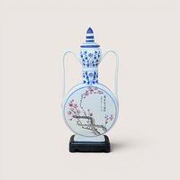 A large blue and white porcelain moon flask with pink plum blossoms and Chinese calligraphy on a wooden stand against a plain background