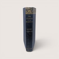The blue spine of a vintage hardcover book featuring ornate gold gilt decorations and lettering on a plain background