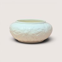 A round cream colored ceramic bowl with embossed poinsettia flowers resting on a light beige background
