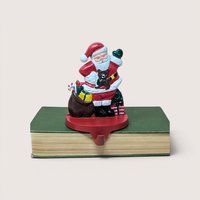 A vintage cast iron Santa Claus stocking holder with a toy sack sitting on a green book against a plain background