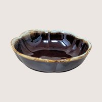 A vintage round fluted ceramic bowl with a glossy dark brown drip glaze edge on a plain background