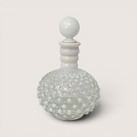 White opalescent hobnail glass cologne bottle with matching round stopper against a plain cream backdrop.
