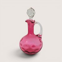 A vintage Fenton cranberry glass coin dot cruet with a clear applied handle and a faceted crystal stopper.