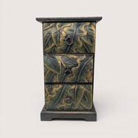 Vertical wooden mini chest with three carved leaf pattern drawers painted in antiqued green and gold with brass ring pulls.