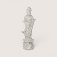 Vintage white porcelain Guan Yin statue standing on a sculpted lotus leaf pedestal base against a light background.