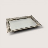 Vintage ornate filigree vanity mirror tray with a detailed metal border set against a plain linen background.