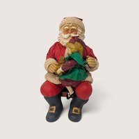 Vintage holiday figurine of Santa Claus sitting on a wooden bench holding a young girl on his lap.