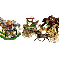 A horizontal view of a set of seven vintage brass-colored metal Christmas ornaments. The collection features a variety of classic equestrian and holiday designs, including several intricate rocking horses, a detailed horse-drawn buggy with a carriage, and other ornate filigree shapes. Each piece has a warm, golden metallic finish with delicate cutout details.