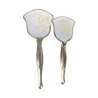 A vertical view of a vintage hand mirror and a matching hairbrush featuring an ornate silver-toned handle and frame. The backs of both pieces feature a white background decorated with a delicate gold-etched pattern of birds perched on flowering branches. The mirror has a wide, scalloped head, while the brush has a matching tapered shape.