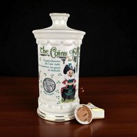 White porcelain whiskey decanter featuring a rectangular silhouette with a tapered neck. Front display includes a colorful leprechaun illustration and various Irish coin graphics. Smooth, glazed ceramic texture with a commemorative poem on the reverse side.