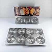 A lot of three silver aluminum baking pans featuring jack-o'-lantern face molds. One pan is a specialized cookie treat pan with stick slots and original cardboard packaging; the other two are matching four-cavity muffin or mini-cake pans.