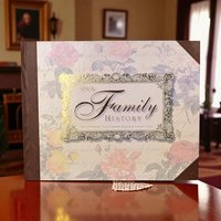 A 1998 "Our Family History" record book and photo album features a floral cover with pink and yellow roses over a scripted background. The central title is enclosed in an ornate gold-foil frame, and the spine and corners are finished with a dark brown leatherette trim. This unused archival book includes sections for a family tree and personal photographs.