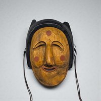 A hand-carved wooden mask with a deep mahogany finish. The face features elongated features, slit eyes, and a prominent nose, with subtle geometric patterns etched along the forehead and cheeks.